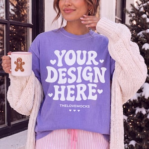 Może przedstawiać: Fioletowy t-shirt z krótkim rękawem z białym napisem YOUR DESIGN HERE i małymi serduszkami, noszony pod kremowym kardiganem o splocie warkoczowym. W dłoni trzymany jest biały kubek z grafiką piernikowego ludzika, widoczne są jasnoróżowe spodnie w paski.