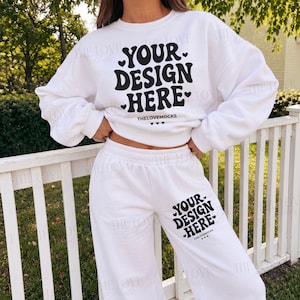 May include: A white long-sleeve crewneck sweatshirt and matching sweatpants set. The sweatshirt features the black text "YOUR DESIGN HERE" with small hearts, and the sweatpants feature the same text and hearts on the left thigh area.