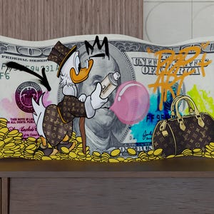 Op de afbeelding: Een rechthoekig wandkunstwerk met een gestileerde cartoon-eend in een jas met patroon en een hoge hoed, die een spuitbus vasthoudt en een roze kauwgombel blaast. De achtergrond is een biljet van honderd dollar met gouden munten en een handtas.