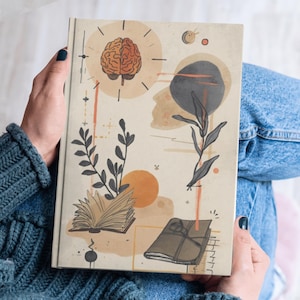 May include: A beige journal with an abstract design featuring a brain, botanical elements, and geometric shapes. The cover art includes a brain illustration, an open book, and a closed book tied with a ribbon. The journal is held by a person wearing a blue sweater.