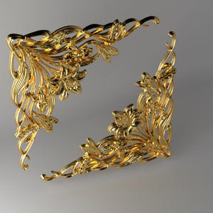 Könnte beinhalten: Zwei passende goldfarbene Metalleckverzierungen mit komplizierten Reliefdesigns aus blühenden Lilien und wirbelndem Blattwerk. Diese dekorativen Stücke haben eine polierte, reflektierende Oberfläche und sind für rechtwinklige Ecken geformt.
