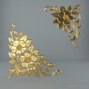 May include: Two ornate, golden floral corner designs. Each features detailed flowers, leaves, and swirling accents. The designs are set against a neutral grey background, highlighting the intricate details of the decorative elements.