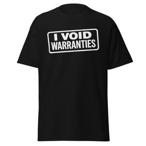 Può includere: T-shirt nero con la scritta bianca "I VOID WARRANTIES" in un carattere invecchiato, racchiusa in un rettangolo bianco. La maglietta è a maniche corte e girocollo.