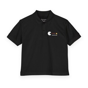 May include: Black polo shirt with a white Pac-Man graphic eating red and yellow dots. The shirt has short sleeves and a collared neckline. The text "Always Eat" is above the Pac-Man graphic.