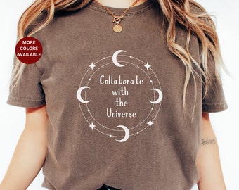 May include: A brown t-shirt with a white graphic design featuring a circle with moons, stars, and the text "Collaborate with the Universe".