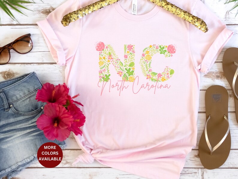 Pu&ograve; includere: Maglietta rosa con le lettere NC in stampa floreale e il testo "North Carolina" sotto.