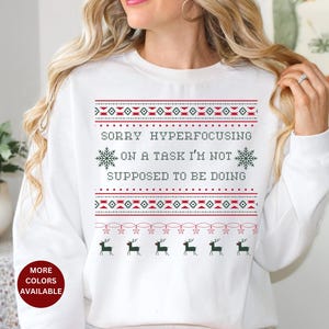 May include: White Christmas sweater with a red and green snowflake pattern and the text "Sorry hyperfocusing on a task I'm not supposed to be doing".