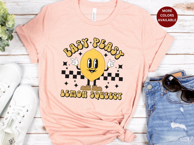 K&ouml;nnte beinhalten: Ein pinkfarbenes T-Shirt mit einem Cartoon-Zitronen-Motiv und dem Text "Easy Peasy Lemon Squeezy".