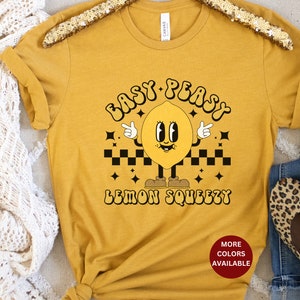 K&ouml;nnte beinhalten: Ein senfgelbes T-Shirt mit einer Retro-Grafik eines l&auml;chelnden Zitronen mit dem Text "Easy Peasy Lemon Squeezy".