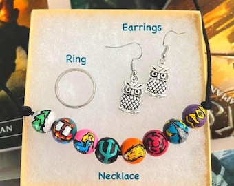 May include: A jewelry set featuring a silver-toned ring, a pair of silver-toned owl earrings, and a necklace with multi-colored beads painted with various symbols. The items are labeled with the text Ring, Earrings, and Necklace.