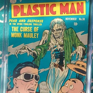 Puede incluir: Un cómic Plastic Man número 38, calificado con 5.0 por CGC, titulado The Curse of Monk Mauley. La portada muestra una figura esquelética de piel verde saliendo de una tumba, con Plastic Man y Woozy Winks mirando con miedo sobre un fondo azul.