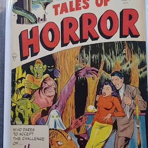 Op de afbeelding: Vintage stripboekcover "Tales of Horror" met een grote rode titel. De illustratie toont een stad die wordt geterroriseerd door een slang, samen met verschillende monsters en een geschrokken stel. De tekst luidt "The Devil's Clock!"