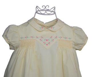Könnte beinhalten: Ein hellgelbes Kleid mit kurzen Puffärmeln, einem Bubikragen mit kleiner rosa Blumenstickerei und einer V-förmigen Passe, die mit rosa Rosenknospen und grünen Blättern bestickt ist, ergänzt durch horizontale Smok-Details auf der Brust.