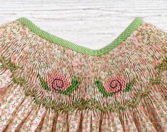 Könnte beinhalten: Ein Kleidungsstück mit rosa Blumenmuster und aufwendigen Handstickereien im Brustbereich. Die Stickerei zeigt rosa Schneckenmotive mit grünen Details, akzentuiert durch einen grün-weiß karierten Besatz am Halsausschnitt.
