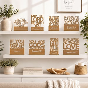 Op de afbeelding: Acht houten tafelbordjes met lasergesneden religieuze teksten en bijbelverwijzingen. Elk bordje staat op een rechthoekige houten voet. De zinnen zijn onder andere In The Morning When I Rise Give Me Jesus, May The Lord Be With You, Blessed Saved Loved By Jesus, Be Strong And Courageous Do Not Be Afraid, If You Love Me Keep My Commands, You Are God's Masterpiece, Putting God First Will Help You Succeed en Let Us Consider How We May Spur One Another On Toward Love And Good Deeds.