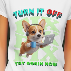 Op de afbeelding: Wit T-shirt met een cartoon corgi met een headset en een laptop en een blauwe mok. Het shirt heeft de tekst "TURN IT OFF" boven de corgi en "TRY AGAIN NOW" eronder. Groene en witte graphics op de achtergrond.