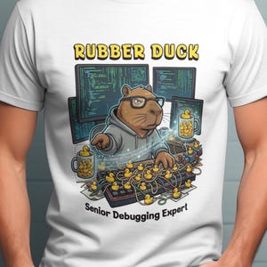 May include: White t-shirt featuring a cartoon capybara wearing glasses and a hoodie, working on a computer with rubber ducks. The text "RUBBER DUCK" is above the image, and "Senior Debugging Expert" is below.