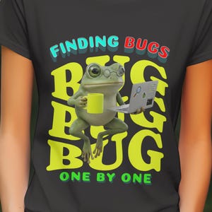May include: Black t-shirt featuring a cartoon frog wearing glasses and holding a yellow mug and a laptop. The shirt has the words "FINDING BUGS" in teal and red, and "BUG" in yellow, with the phrase "ONE BY ONE".