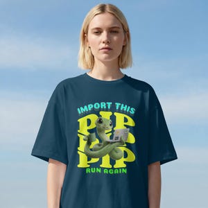 May include: Navy blue t-shirt featuring a green snake graphic with a laptop and coffee cup. The text "IMPORT THIS PIP RUN AGAIN" is in yellow and teal. The shirt is worn by a person.