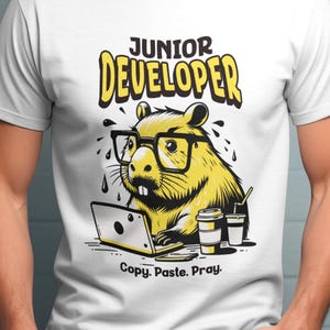 May include: White t-shirt with a yellow cartoon beaver wearing glasses and working on a laptop. The text "JUNIOR DEVELOPER" is above the beaver, and "Copy. Paste. Pray." is below.