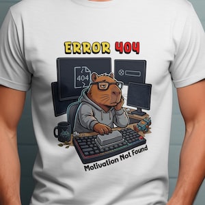 May include: White t-shirt with a cartoon capybara wearing glasses and a hoodie, sat at a computer with the text "ERROR 404" and "Motivation Not Found". The capybara is surrounded by computer monitors and a keyboard.