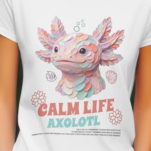 Könnte beinhalten: Weißes T-Shirt mit einer Illustration eines Axolotl in Pastellfarben. Der Axolotl ist in Rosa-, Blau- und Pfirsichtönen dargestellt. Der Text "CALM LIFE AXOLOTL" ist darunter gedruckt, zusammen mit weiterem Text.