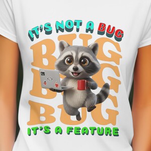 Peut inclure: T-shirt blanc avec un raton laveur de dessin animé tenant un ordinateur portable et une tasse rouge. Le texte sur le t-shirt se lit "IT'S NOT A BUG, IT'S A FEATURE" en vert, orange et rouge. Le raton laveur est gris et blanc.