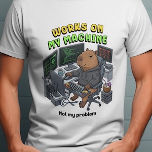 May include: White t-shirt with a cartoon capybara in a hoodie at a computer desk. The text "WORKS ON MY MACHINE" is above the capybara, and "Not my problem" is below. The design is in a cartoon style.