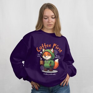 Könnte beinhalten: Ein dunkelvioletter Pullover mit dem Text "Coffee First" in Orange. Der Pullover zeigt einen Cartoon-Fuchs mit grünem Kapuzenpullover und einer Kaffeetasse. Der Text "Then Code" und "Maybe Meetings" sind ebenfalls vorhanden.