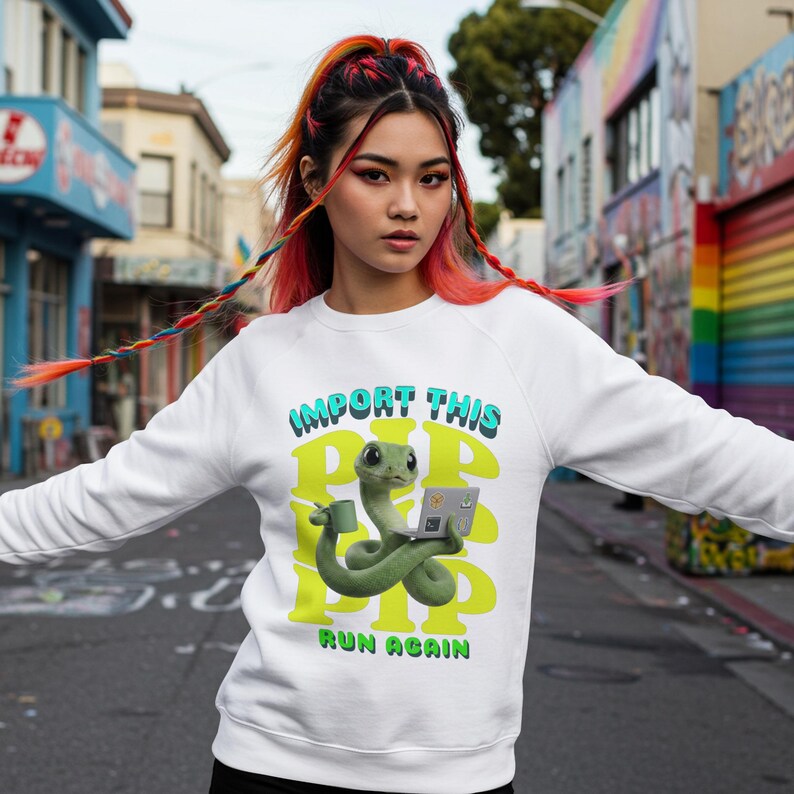 May include: White sweatshirt featuring a green snake graphic with a coffee cup and laptop. The text "IMPORT THIS PIP PIP PIP RUN AGAIN" is printed in green and blue. The sweatshirt is worn by a person with colourful hair.