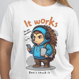 May include: White t-shirt featuring a cartoon hedgehog wearing a blue hoodie, headphones, and a backpack, holding a phone and a laptop. Text reads "It works" and "Don't touch it". The hedgehog has a serious expression.