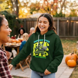 May include: A dark green hoodie with white drawstrings and a graphic of a green snake holding a laptop. The text on the hoodie reads "IMPORT THIS PIP PIP RUN AGAIN" in a combination of white and yellow.