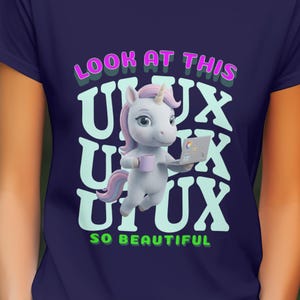May include: Navy blue t-shirt with a cartoon unicorn holding a mug and laptop. The text on the shirt reads "LOOK AT THIS UX UX UX SO BEAUTIFUL" in pink and green lettering. The unicorn has a pink mane and tail.