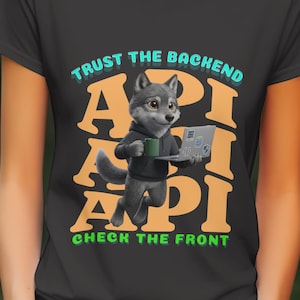 Op de afbeelding: Zwart T-shirt met een cartoonwolf die een mok en een laptop vasthoudt. Het ontwerp bevat de tekst "TRUST THE BACKEND" en "CHECK THE FRONT" met het woord "API" in grote oranje letters.