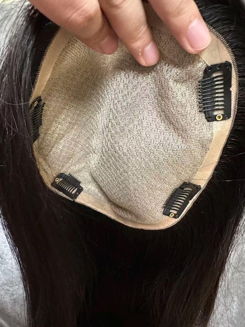 May include: A dark brown hair topper with a beige mesh base and several black clips for attachment. The hair is long and straight, with a natural appearance. The topper is designed to add volume and coverage.