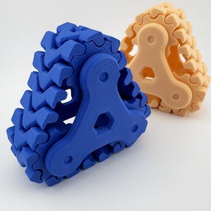 May include: Two 3D-printed, interlocking gear-like structures. One is blue, the other is a light orange. Each has a central, triangular hub with a hexagonal opening. The blue gear is in the foreground, with the orange gear behind it.