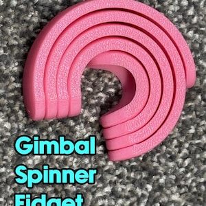 May include: A pink gimbal spinner fidget toy. The toy is made of a soft material and has a curved design. The text "Gimbal Spinner Fidget" is displayed in a teal font.