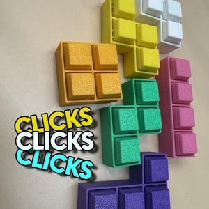 May include: A selection of colourful, textured, Tetris-shaped blocks in yellow, white, green, pink, orange, and purple. The word "CLICKS" is displayed in a layered, stylised font. The blocks are arranged in various configurations.