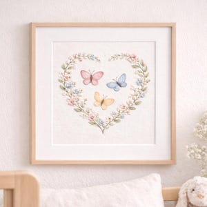 Könnte beinhalten: Gerahmtes Kunstwerk mit einem herzförmigen Blumenkranz und drei Schmetterlingen in Rosa, Blau und Gelb. Das Stück befindet sich in einem hellen Holzrahmen, ideal für ein Kinderzimmer oder eine Heimdekoration.