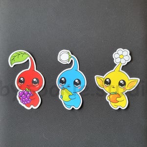 May include: A gray binder with the word "bindrz" printed on the front. Three colorful cartoon stickers are affixed to the binder: a red character holding grapes, a blue character holding a pear, and a yellow character with a flower.