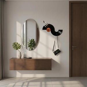 May include: A contemporary hallway scene with a floating wooden console, an oval mirror, and a coat rack crafted from a vinyl record. A small black handbag hangs from the record coat rack. The console is approximately 150 cm in length.