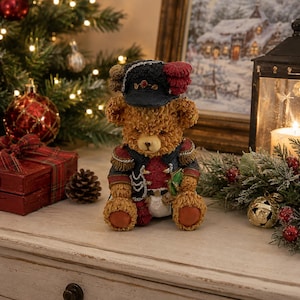 May include: A brown teddy bear figurine dressed in a dark blue military-style uniform with gold trim, epaulets, and a black hat featuring a red plume. The bear has textured fur, a light-coloured muzzle, and is seated in a forward-facing position.