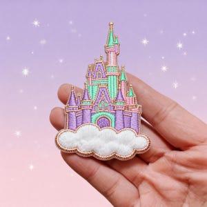 May include: An embroidered patch featuring a fairy tale castle with purple, mint green, and pink towers, resting on a fluffy white cloud base. The entire design is outlined with a metallic gold thread, creating a detailed and textured appearance.
