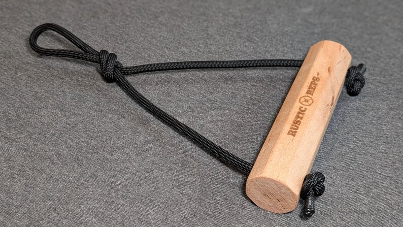 May include: A light-colored wooden handle with the text "RUSTIC REPS-" is connected to a black rope loop. The handle has a hexagonal shape. The rope is knotted at both ends of the handle.