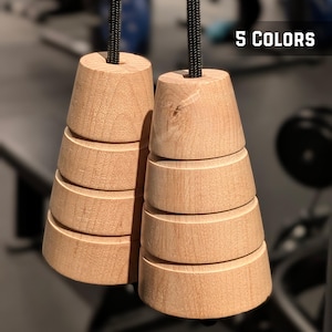 Puede incluir: Dos mangos de madera de color claro con forma cónica y escalonada, cada uno unido a un cordón trenzado negro. El texto 5 COLORS es visible en la esquina superior derecha. Los mangos presentan un acabado de madera natural y diseño cilíndrico.