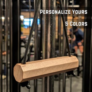 May include: A light brown wooden gym cable attachment handle with an octagonal cross-section, suspended by a black braided rope. The text "PERSONALIZE YOURS" and "5 COLORS" is displayed in white lettering against the dark background.