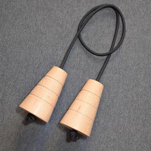 May include: A wooden jump rope with light brown handles and a black rope. The handles are cone-shaped with horizontal grooves and a small black knot at the bottom. The rope is looped at the top.