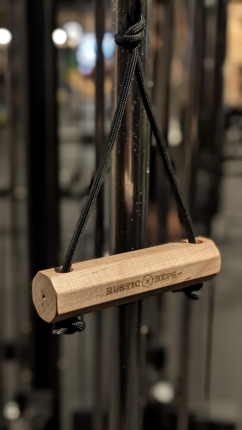 A solid Maple wood grip in an octagonal prism shape hanging form a cable machine in the gym. This version features two ends of paracord run through the bar to help resist rotation while pulling allowing you to focus on max weight.