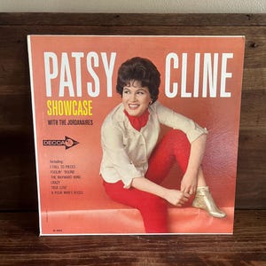 May include: A square vinyl record cover featuring Patsy Cline Showcase with The Jordanaires. The cover is orange with white text, showing a smiling person in a white collared shirt, red pants, and gold boots. It lists songs including I Fall to Pieces.