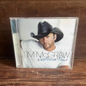 May include: A music CD in a clear plastic jewel case featuring the album Southern Voice by Tim McGraw. The cover art displays a man wearing a black cowboy hat and a white t-shirt against a plain white background, with the artist and album title text.